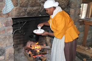 Clifton places chicken to cook in a cast iron pot over an open hearth.