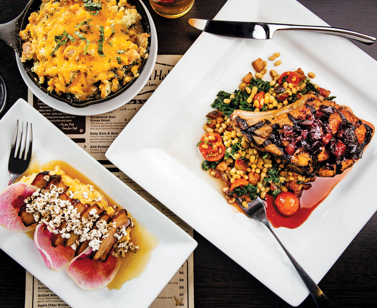 Clockwise from top: Cheddar spoon bread with house-cured bacon; grilled pork chop, field pea ragout, and sautéed kale with Cheerwine redeye gravy; pork belly and grits with a bourbon-sorghum glaze and popped sorghum grain.