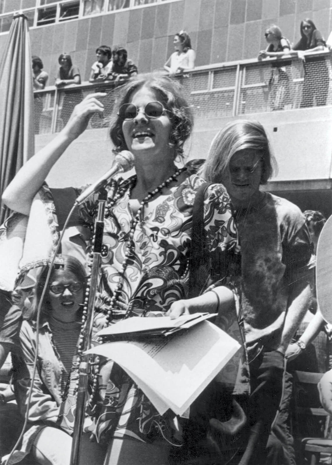 Cathy Sterling standing at microphone while other students surround her.