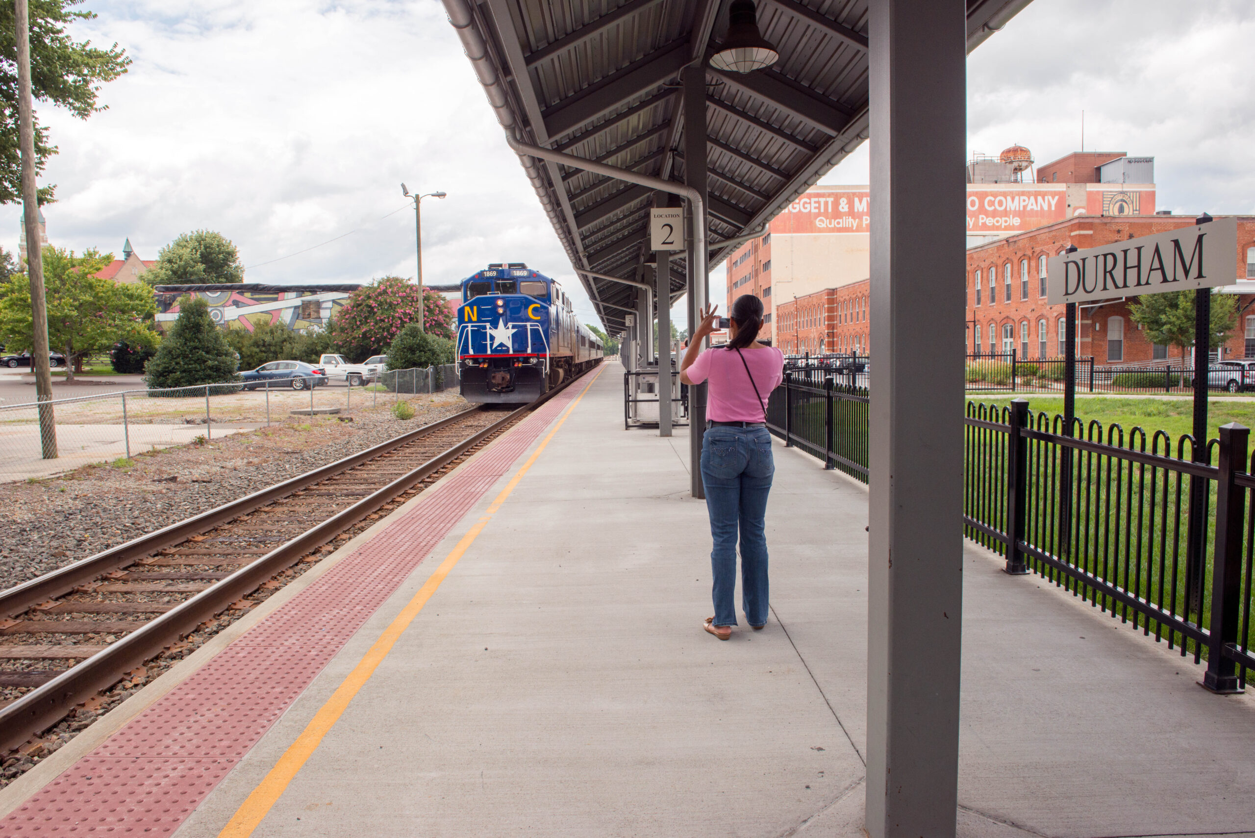 Woman stands on the platform at Durham station to take photo of arriving train.