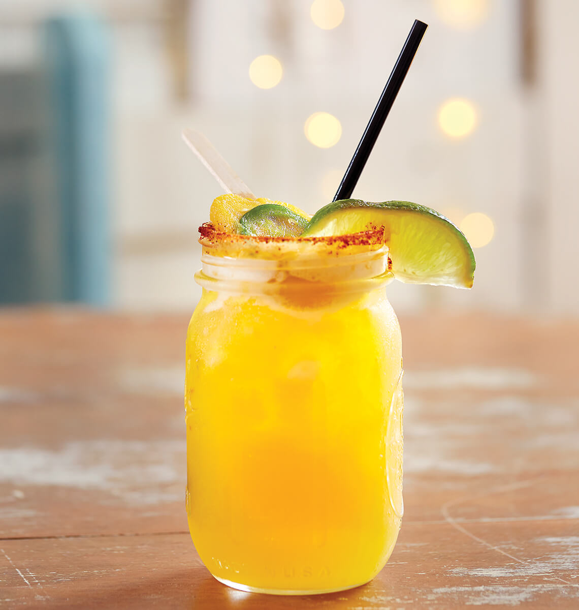 Fancy cocktail in a mason jar with fruit garnish.