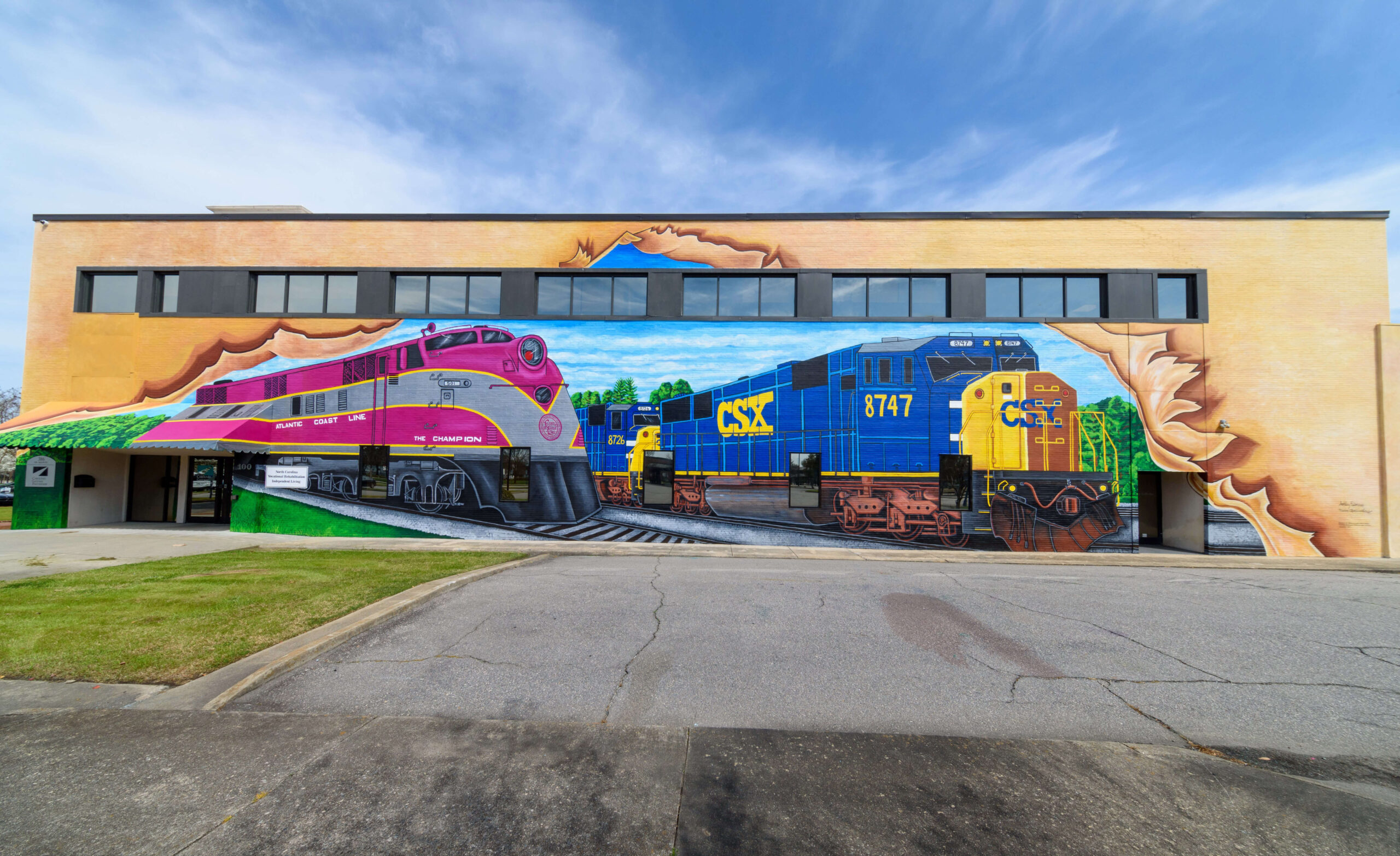 Colorful mural of 2 trains painted on the side of the Carolinas Gateways Partnership building across from the Rocky Mount train station.