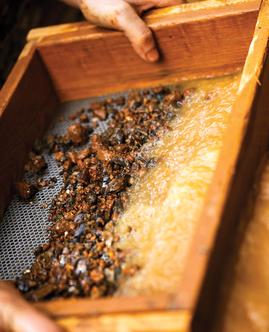 Hands process rocks through a sifting tray.
