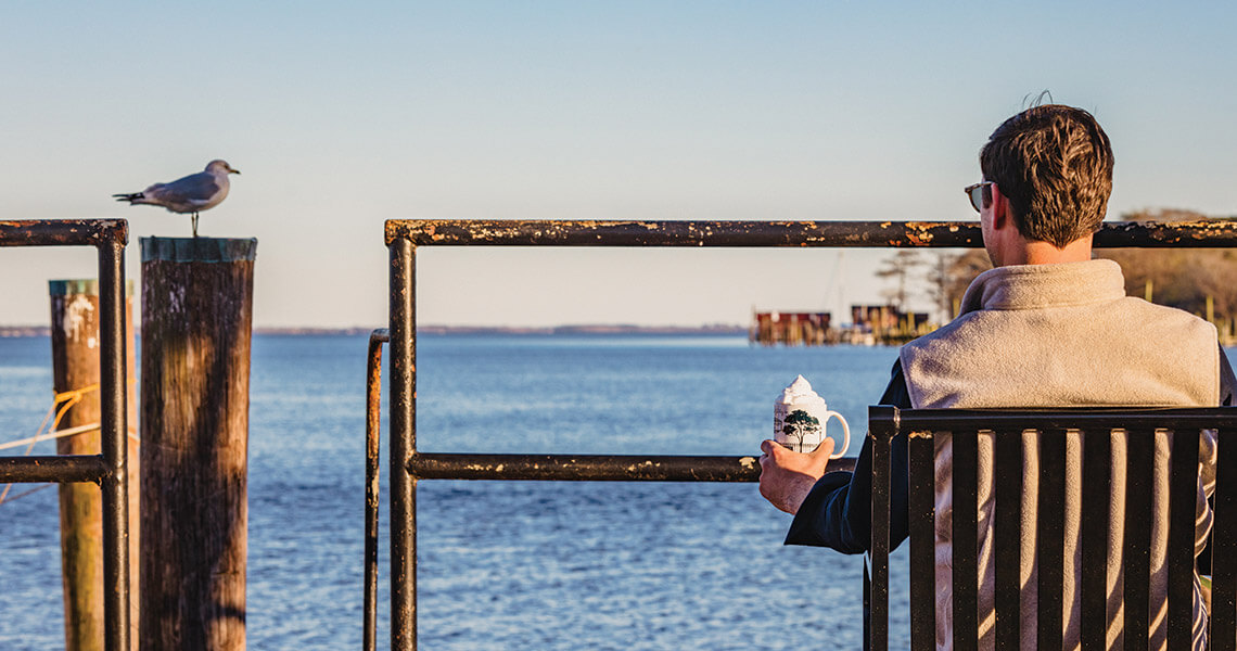 Man drinks hot chocolate while overlooking the Pasquotank River.