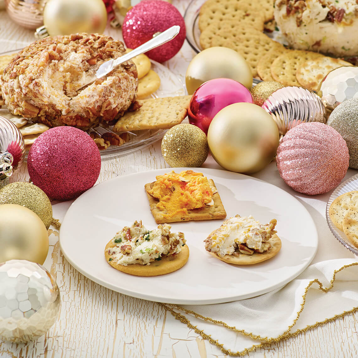 Table with Christmas tree ornaments, a cheese ball, and crackers topped with cheese spread.