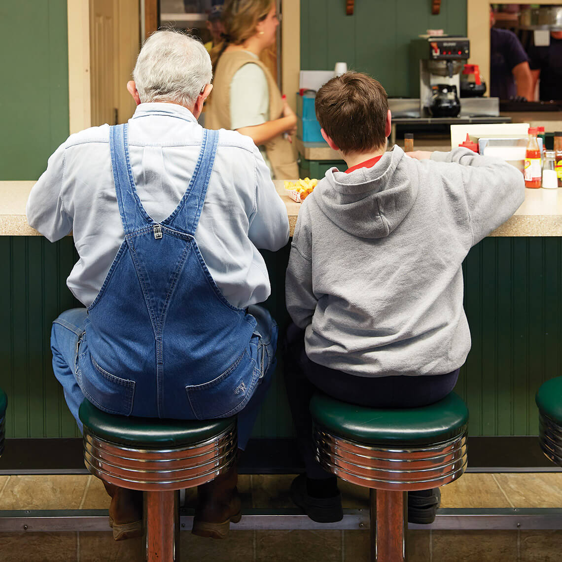 Grandfather and grandson sit at on the green stools at the counter at Lexington Barbecue