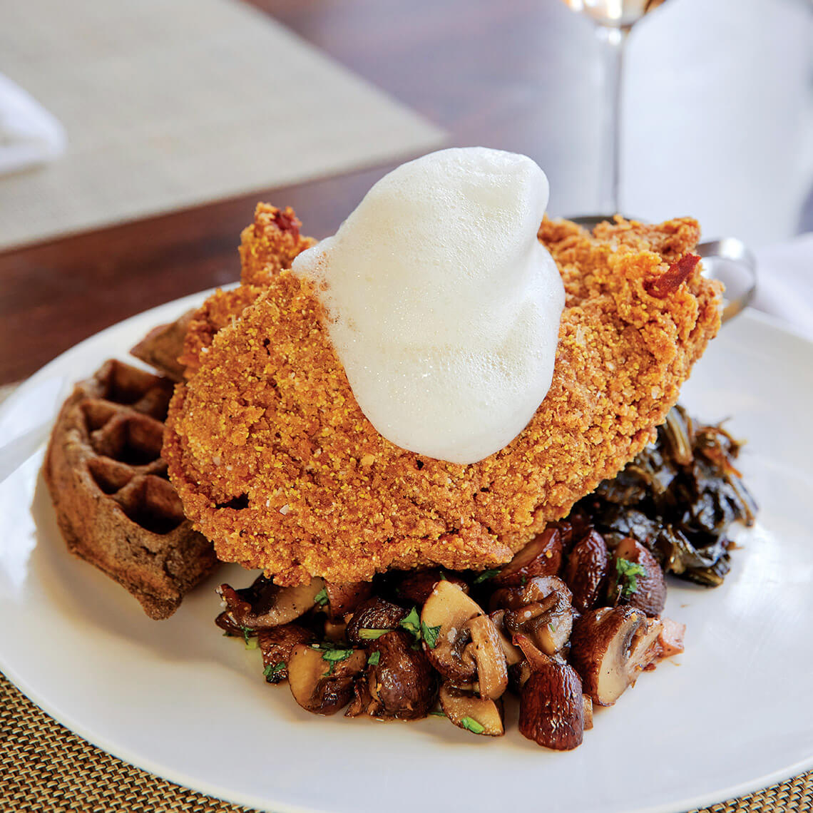 Joyce Farms chicken and serves it over a buttermilk buckwheat waffle with collards, sautéed mushrooms, and a bacon-mushroom emulsion.
