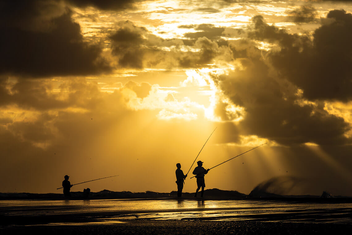 Silhouetted anglers against the sunrise at Cape Point welcome a morning of North Carolina fishing.