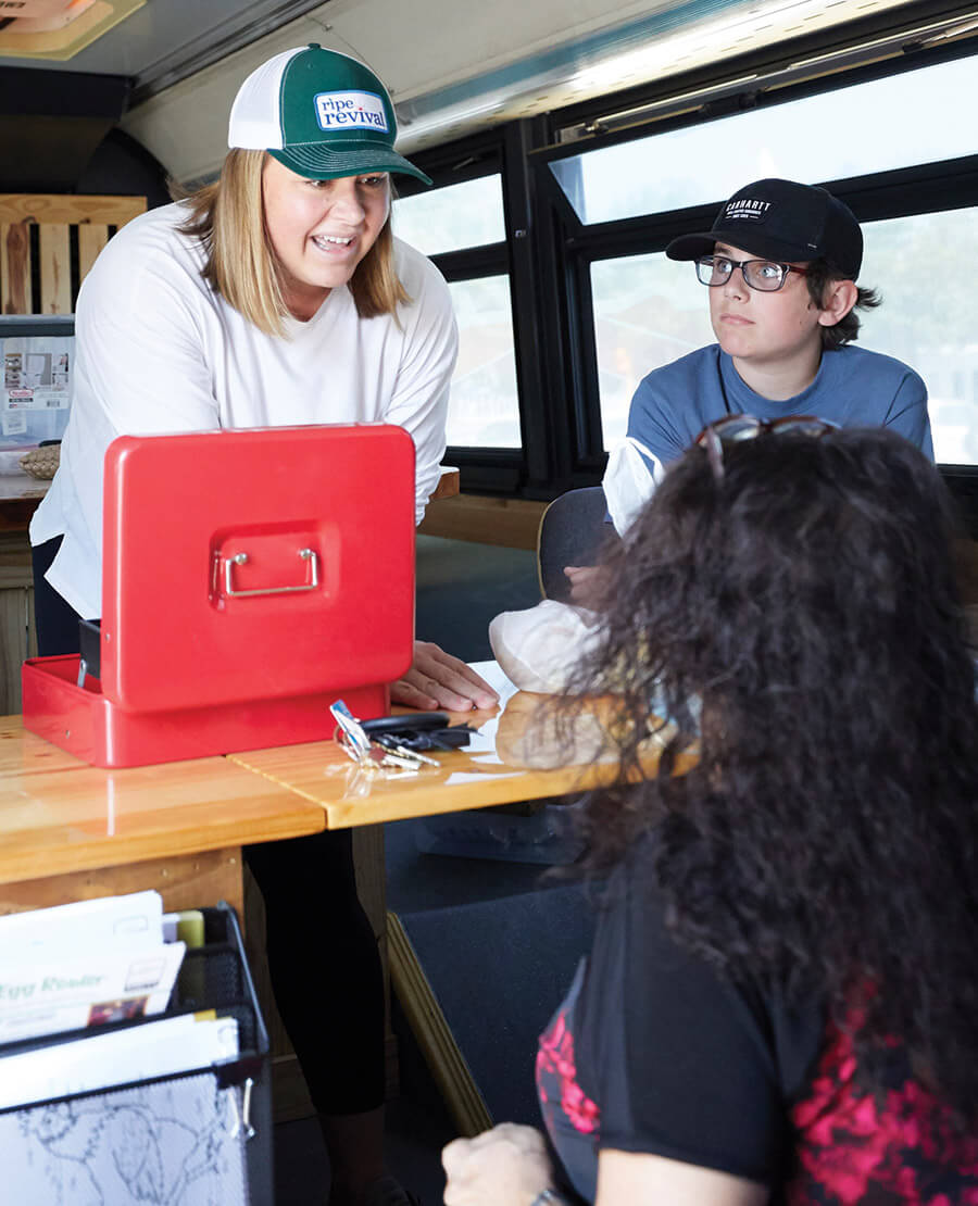 Ripe Revival volunteer works the cash box as customers buy produce on the mobile market bus