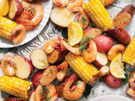 Shrimp boil contents, including shrimp, corn, sausage, and potatoes, laid over sheets of newspaper