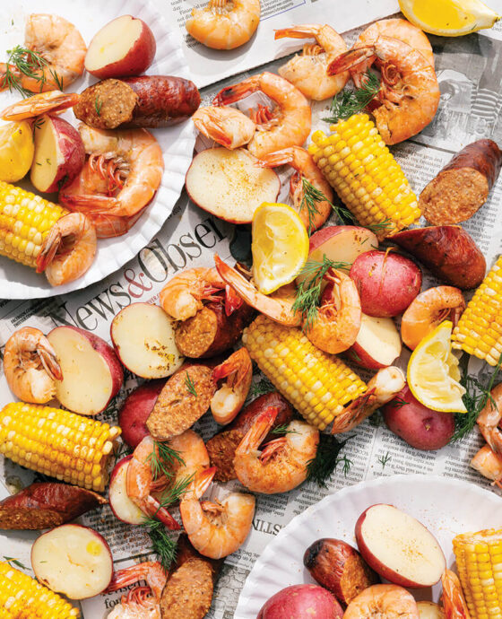 Shrimp boil contents, including shrimp, corn, sausage, and potatoes, laid over sheets of newspaper