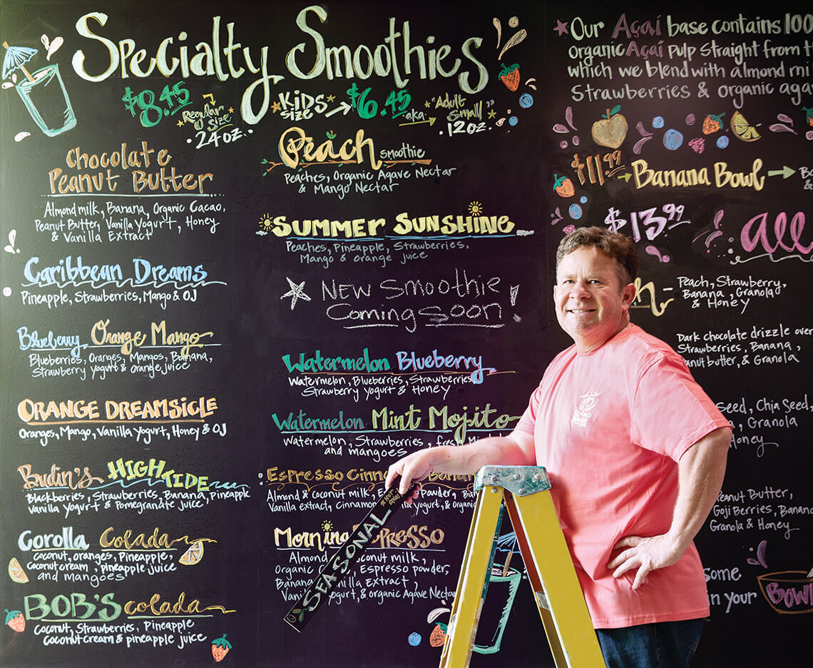 Doug Kraus in front of chalkboard menu at Island Smoothie Cafe