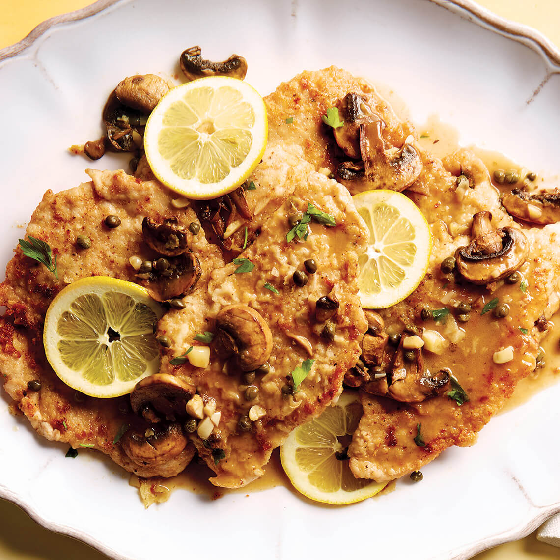 Veal piccata on a plate with lemon slices and mushrooms