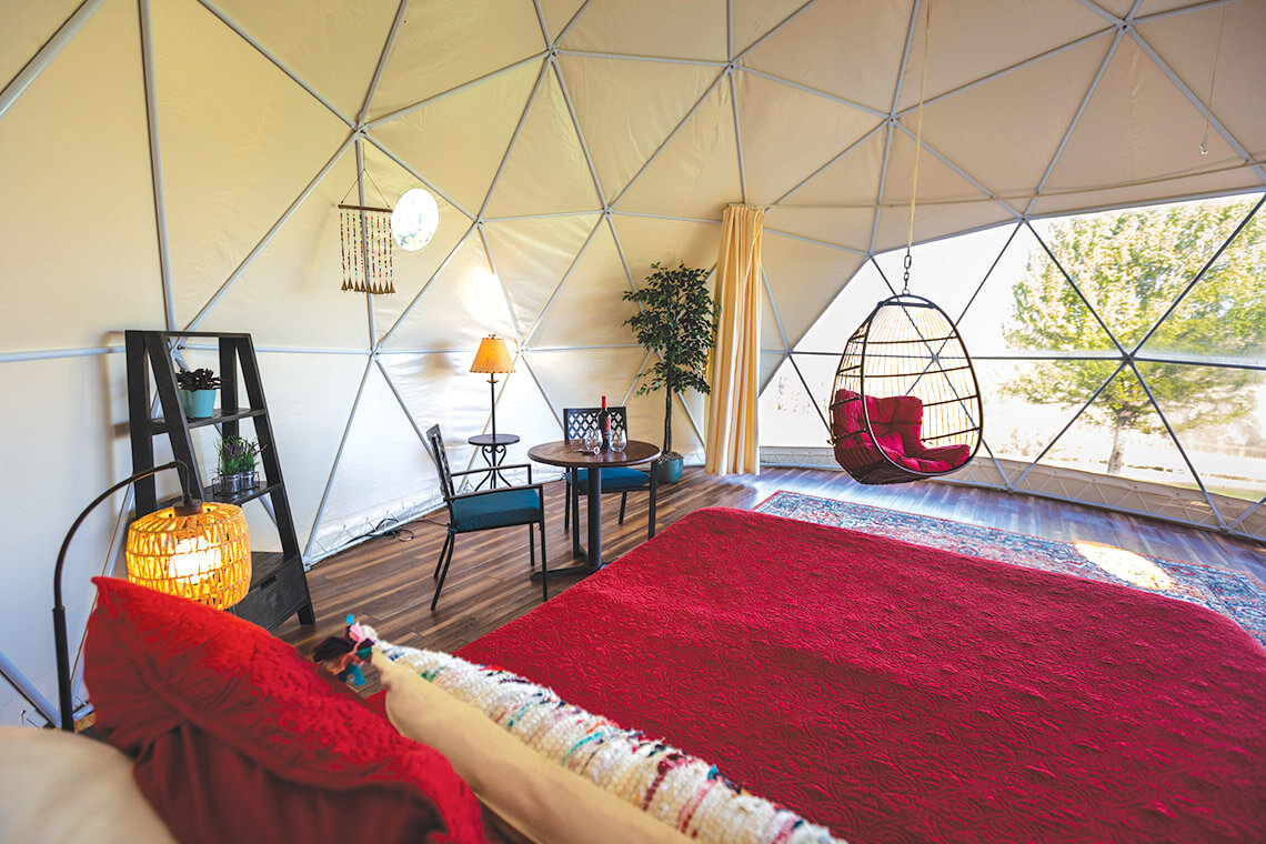 The glamping tent with a bed, swinging chair, lamps, and other curtains
