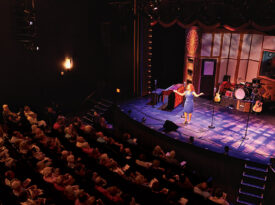 Peggy Taphorn greets the audience from the stage at the Temple Theatre