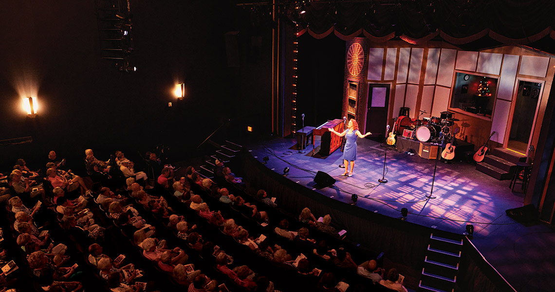 Peggy Taphorn greets the audience from the stage at the Temple Theatre