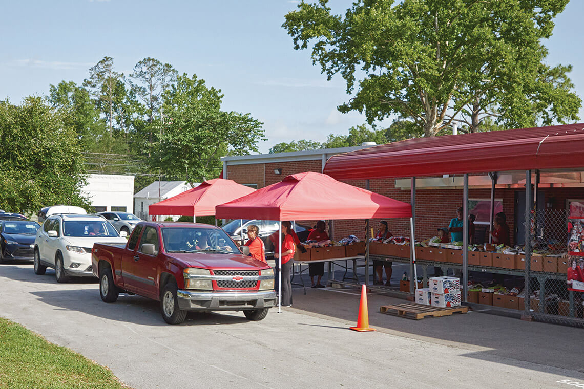 Cars roll through the drive-through pantry and receive food from volunteers