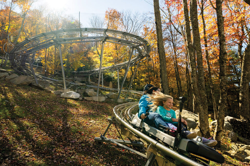 Family riding the Wilderness Run Alpine Coaster through fall foliage