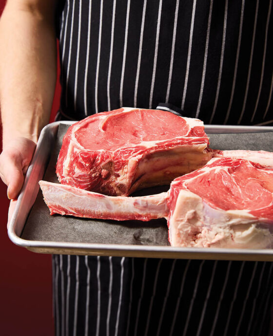Zev Flinchum holds tray of tomahawk rib eyes