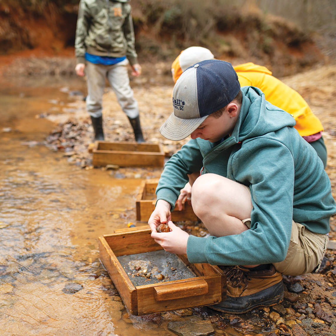 Visitors to Hiddenite sluice their finds in the creek bed.