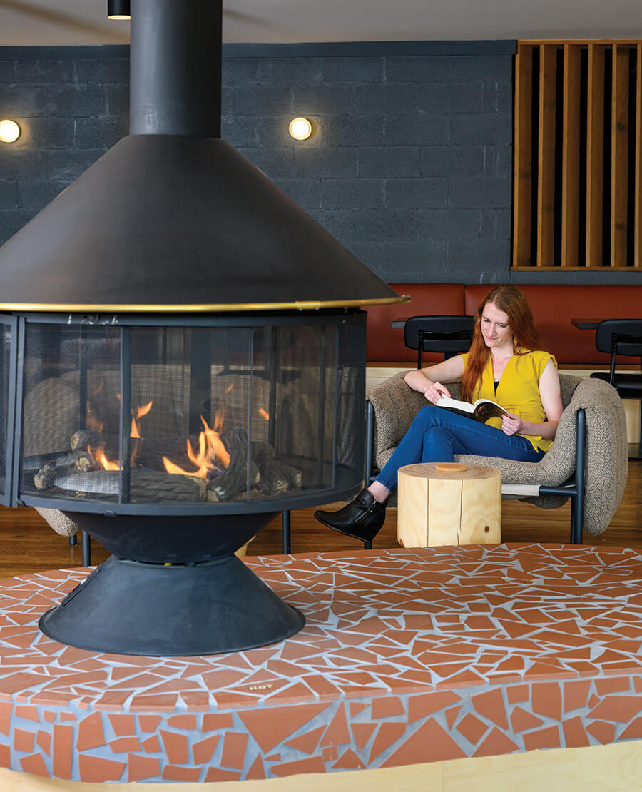 Woman reads by circular fireplace at Rhode's Motor Lodge