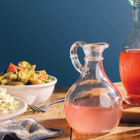 Assorted jars of vinegars on a table with barbecue and vegetables