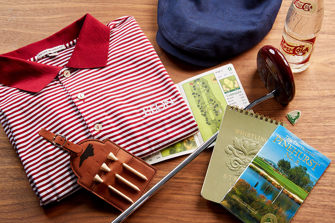 Golf paraphenalia belonging to the author's father, including an Elon golf shirt, a ceramic putter, an antique Pepsi bottle, and yardage books. 
