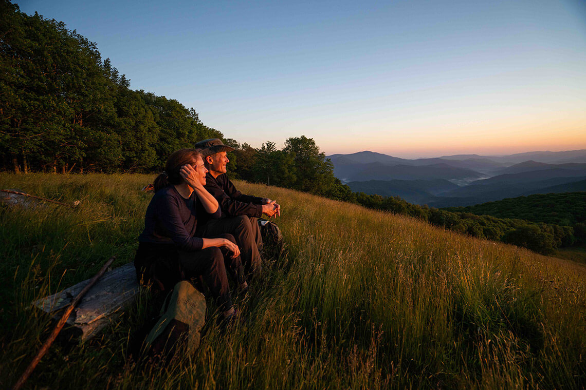 Hikers watch the sunset on top of a mountain bald. 