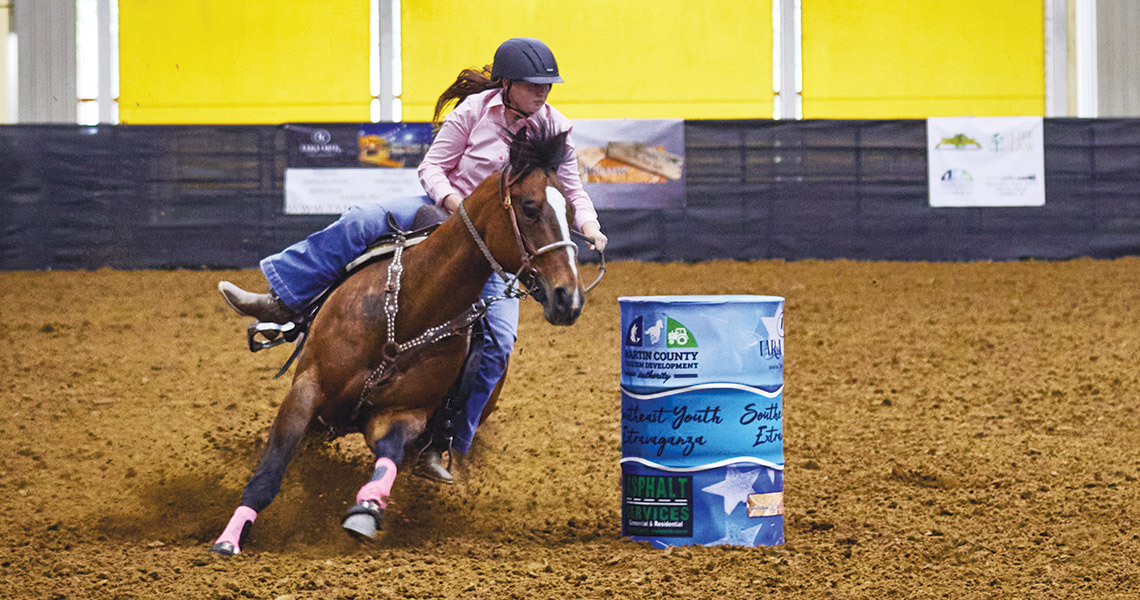 Young woman guides a horse around barrels at the Senator Bob Martin Agricultural Center