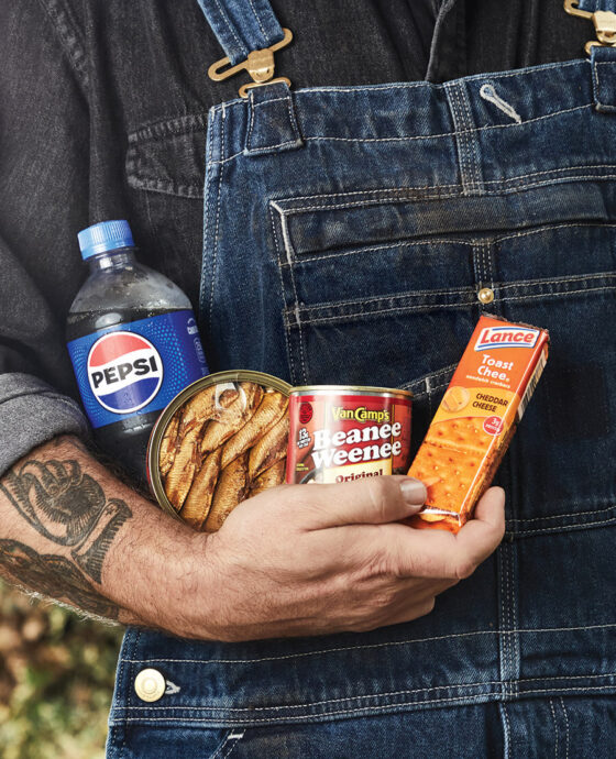 Man holding Pepsi, tinned fish, beanie weenies, and Nabs
