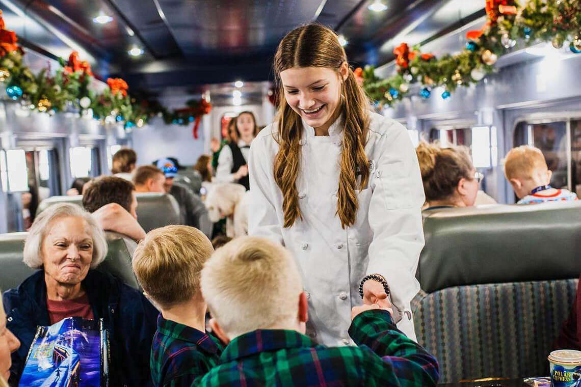 Woman and children dance in a train car on the Polar Express ride.