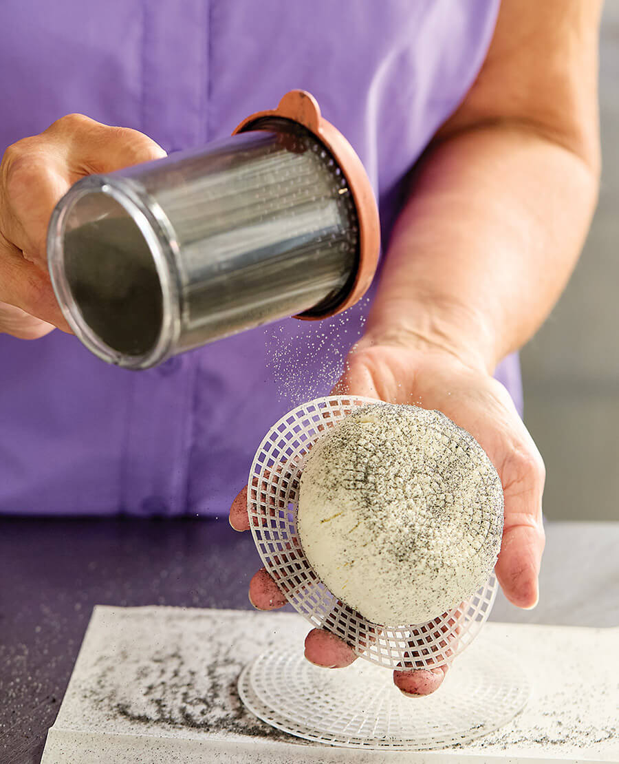 Chris dusts a cheese with ash at Spinning Spider Creamery