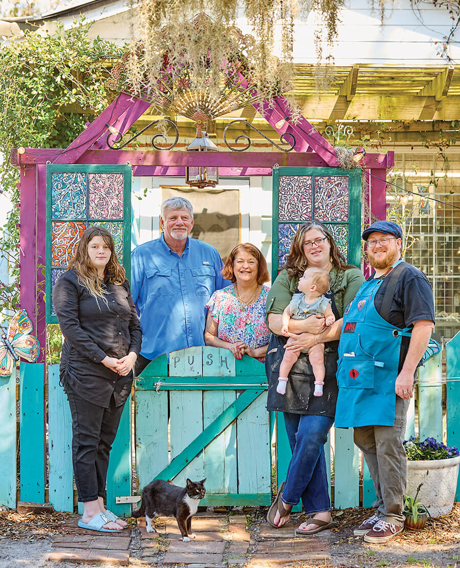 Minnie, a community cat available for adoption, poses with the Keith family — (from left) Grae, Richard, Beth, Kate holding baby Marigold, and Chris Choyce in front of Wild Rose Glass